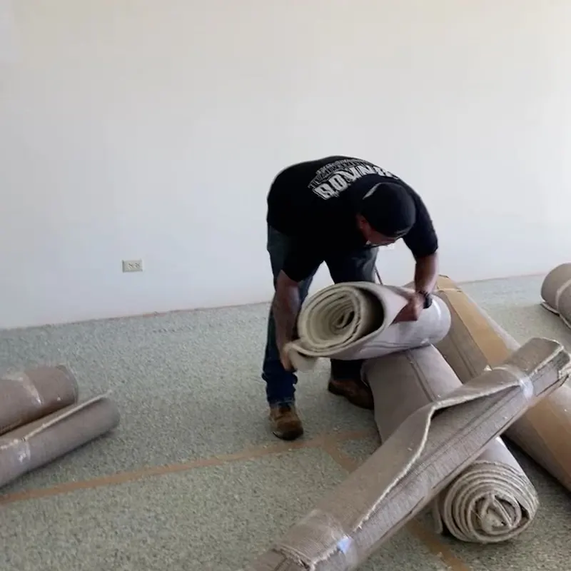 A crew member rolling up old carpet in an emptied room during a demo job.