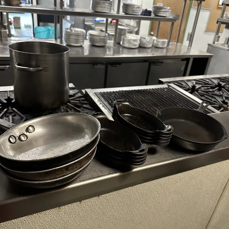 A commercial kitchen counter stacked with pans and stockpots waiting to be cleared out.