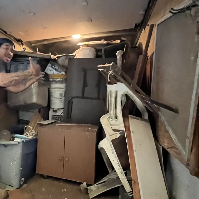The back of the box truck part-loaded with a cabinet, buckets, a bin and broken timber, a crew member working at the tailgate.